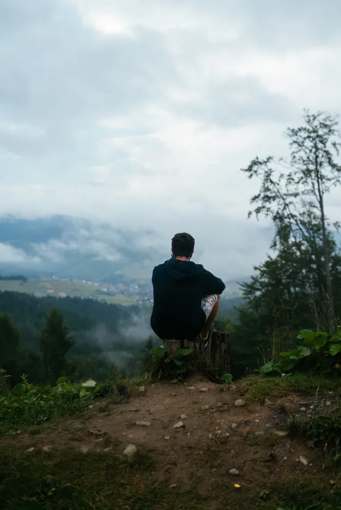 Ein Mann hockt auf einem Baumstump auf einem Berg und geniesst die Aussicht auf die Wolken im Tal