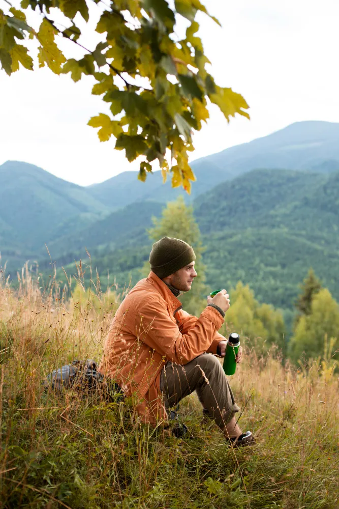 Mann sitzt in einer Wiese in den Berge und macht Pause mit Kaffee